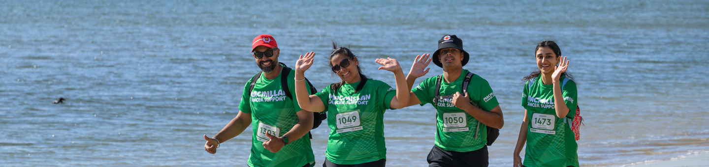 Two men and two women hiking on the beach wearing their Macmillan t-shirts