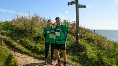 A man and a woman standing in front of a coastal signpost wearing their Macmillan t-shirts