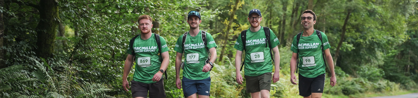 Four men wearing their Macmillan Mighty Hike t-shirts walking down a road.