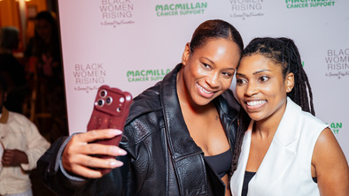 Two women pose together in front of a Black Women Rising and Macmillan Cancer Support event backdrop.