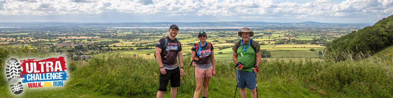 Three people are standing together in a field. Behind them is a view of the valley below.