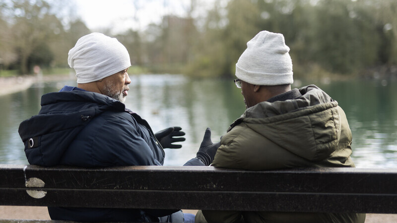 Two people walk side by side across a wooden bridge in a park, demonstrating the benefits of companionship and staying active outdoors.