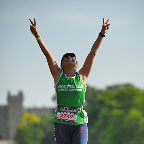 A triathlon participant is celebrating and has their arms raised up above their head. They are doing peace signs. 