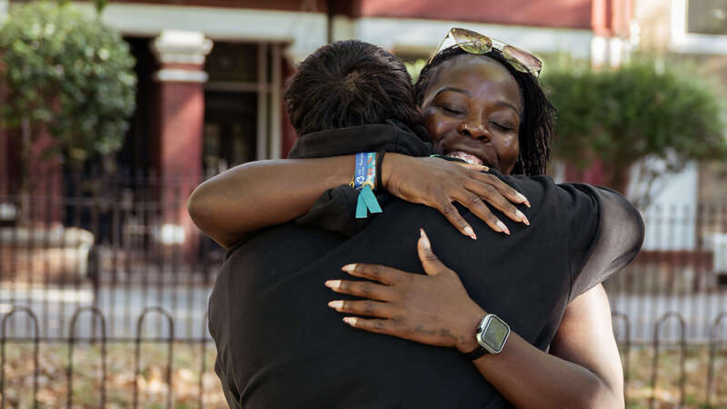 Two people share a warm embrace in a park surrounded by trees and autumn leaves, reflecting connection and community.