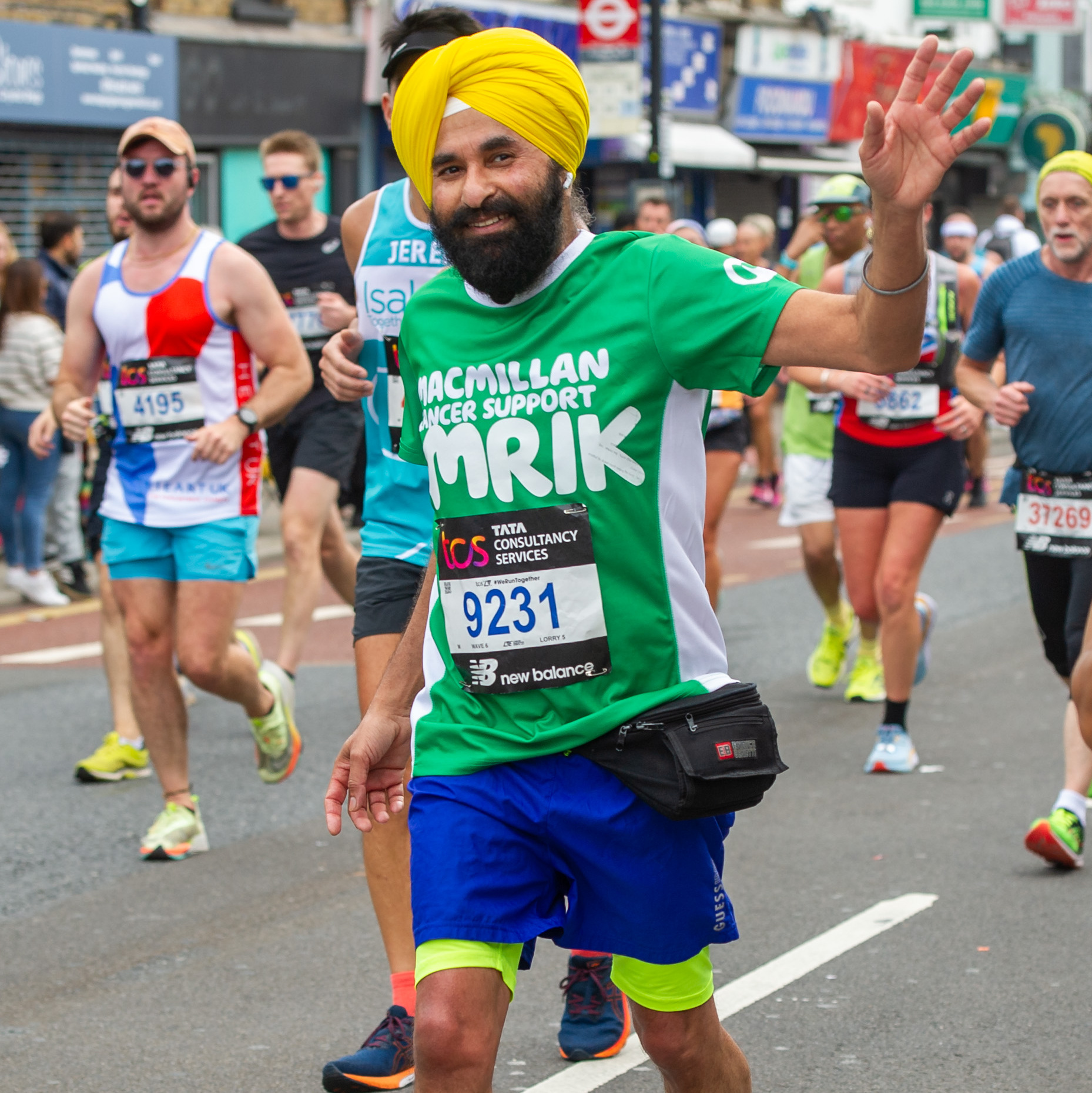 A man in a bright yellow turban running the London Marathon and waving