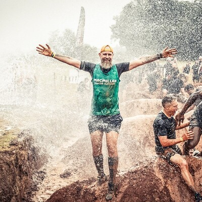 A man wearing a Macmillan vest getting sprayed with water in the mud