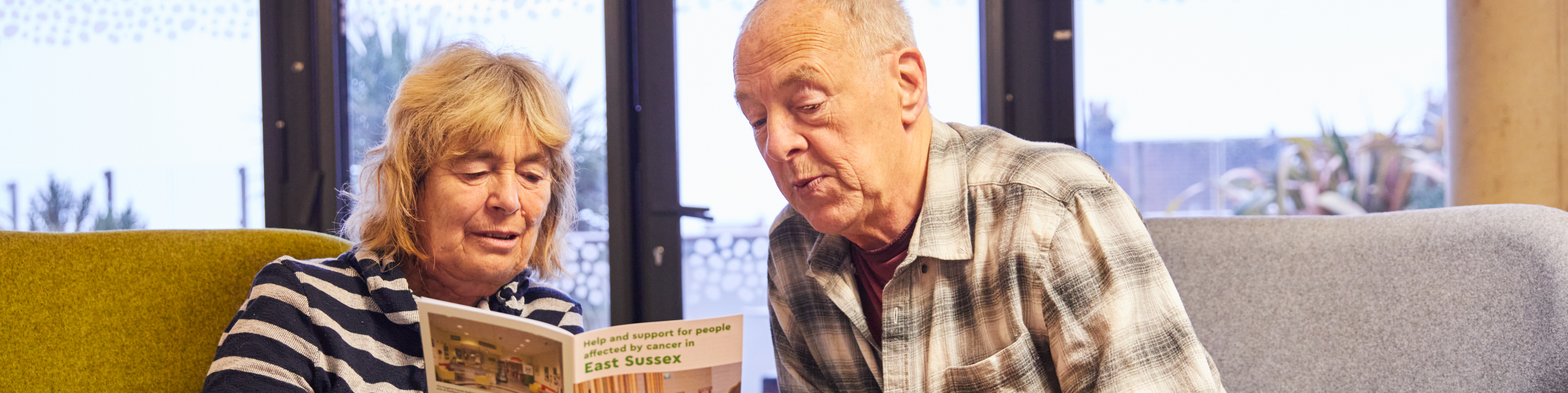 Two people looking at a cancer information booklet together. In front of them is a small table with mugs.