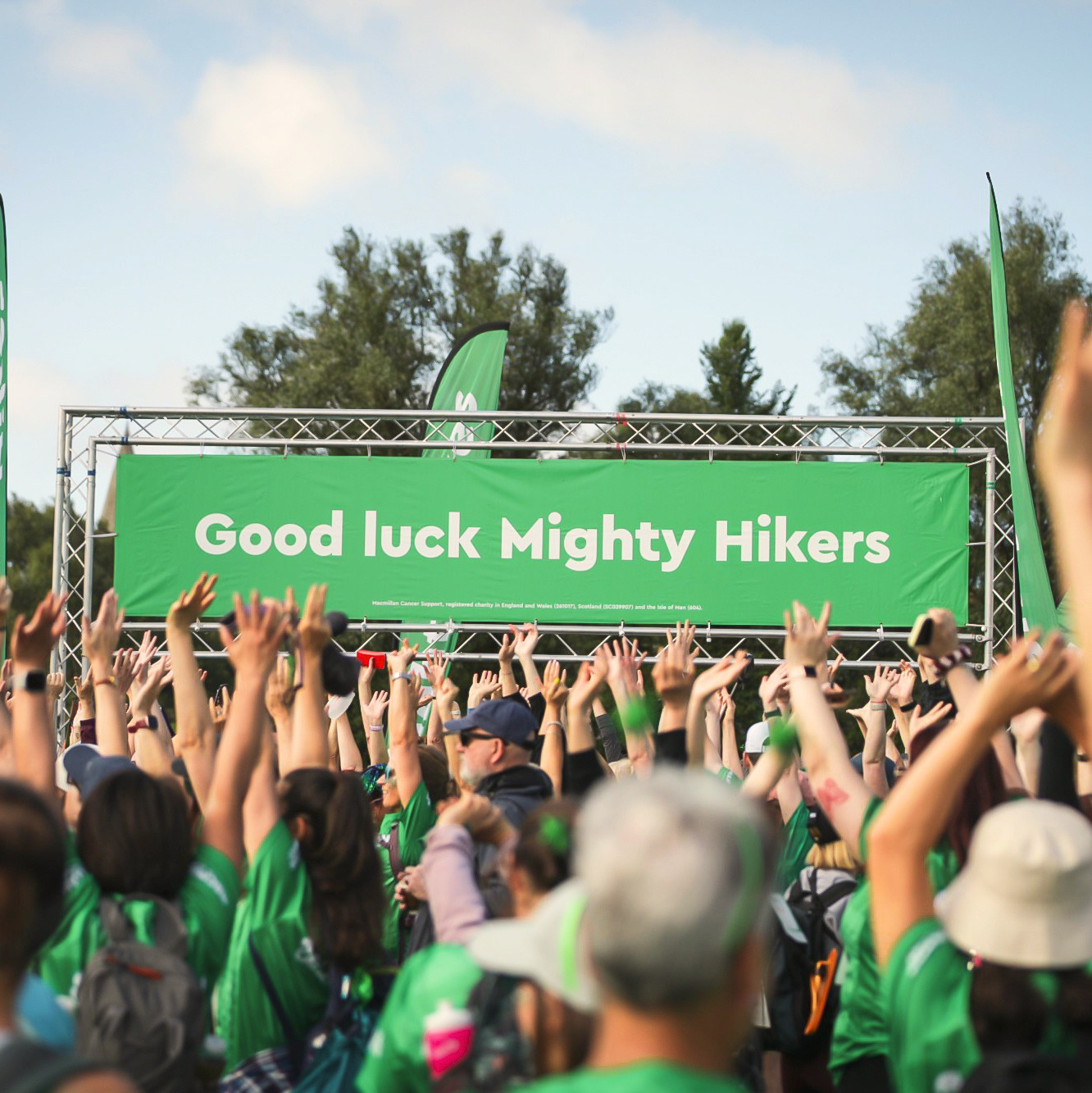 A crowd of people celebrating at a Mighty Hikes event. Their arms are in the air and in the distance is a banner that states: Good Luck Mighty Hikers.