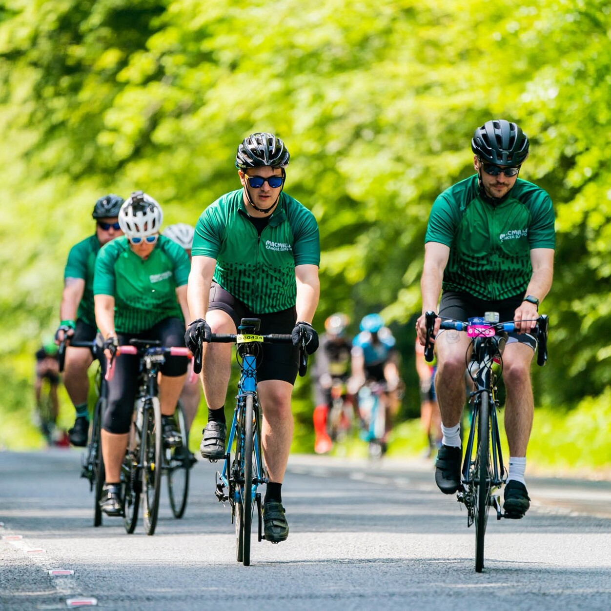 A group of cyclists all wearing green Macmillan cycling jerseys