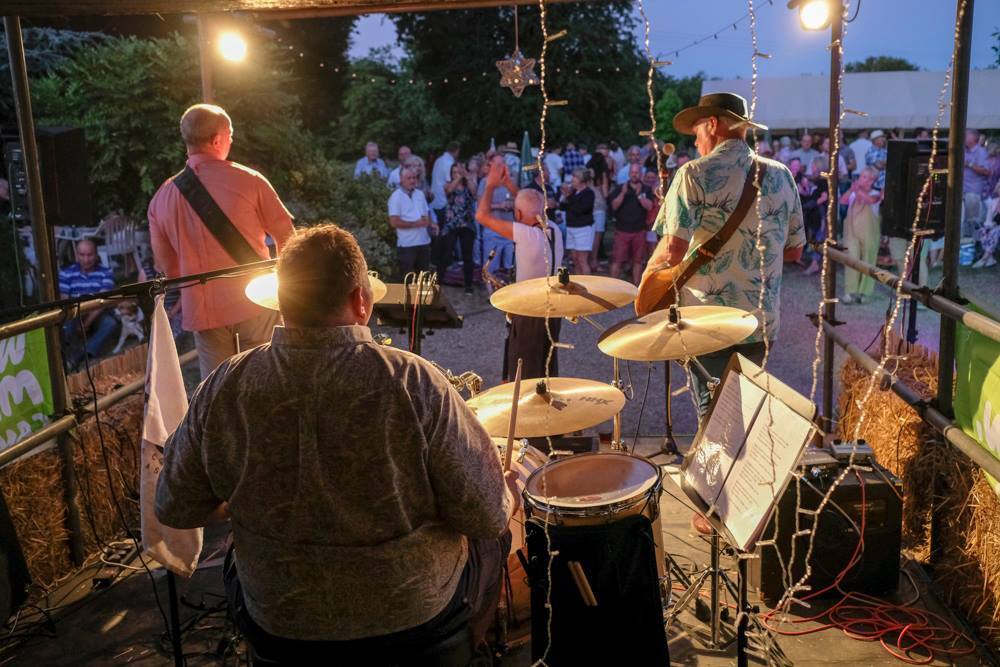 View from the back of a stage at a music event looking towards the crowd. There is a drummer and two men at the front playing guitars.