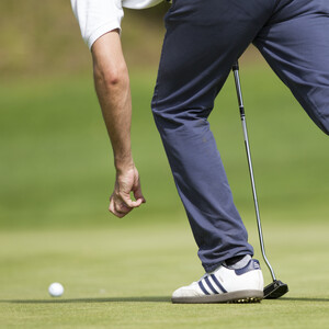 A golfer leans over to pick up a golf ball on a putting green