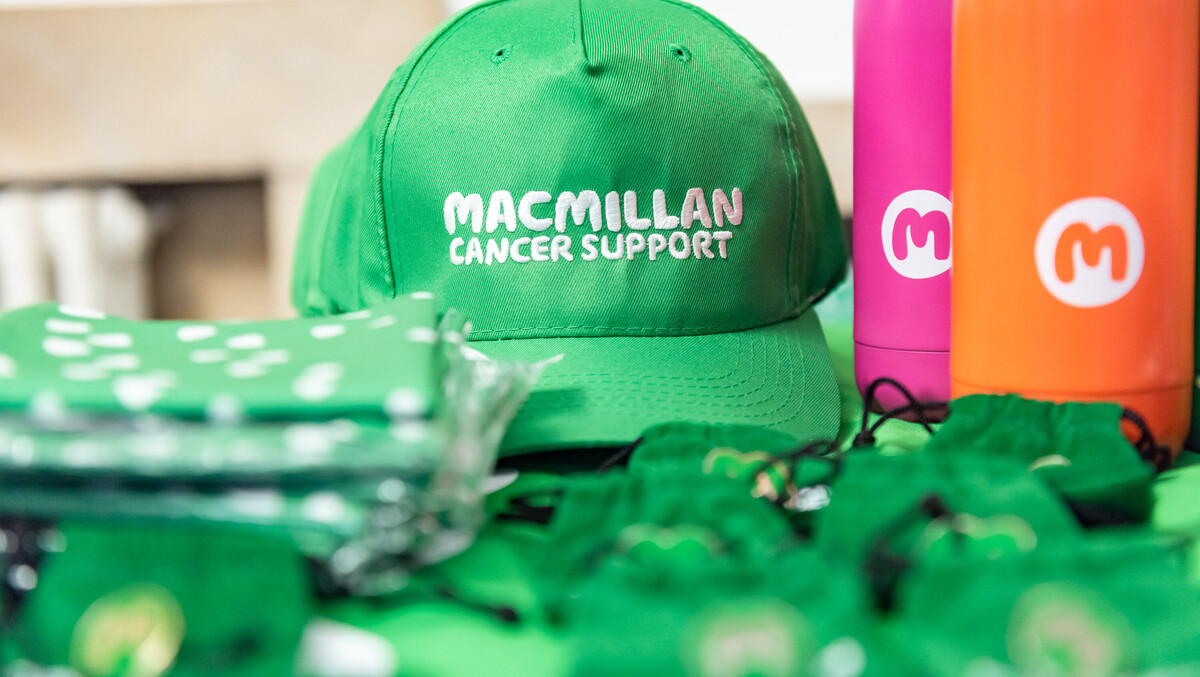A table of Macmillan branded merchandise including caps, metal water bottles, and folded t-shirts.