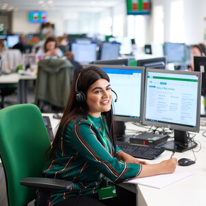 A woman sitting in front of a computer wearing a microphone headset talking to someone.