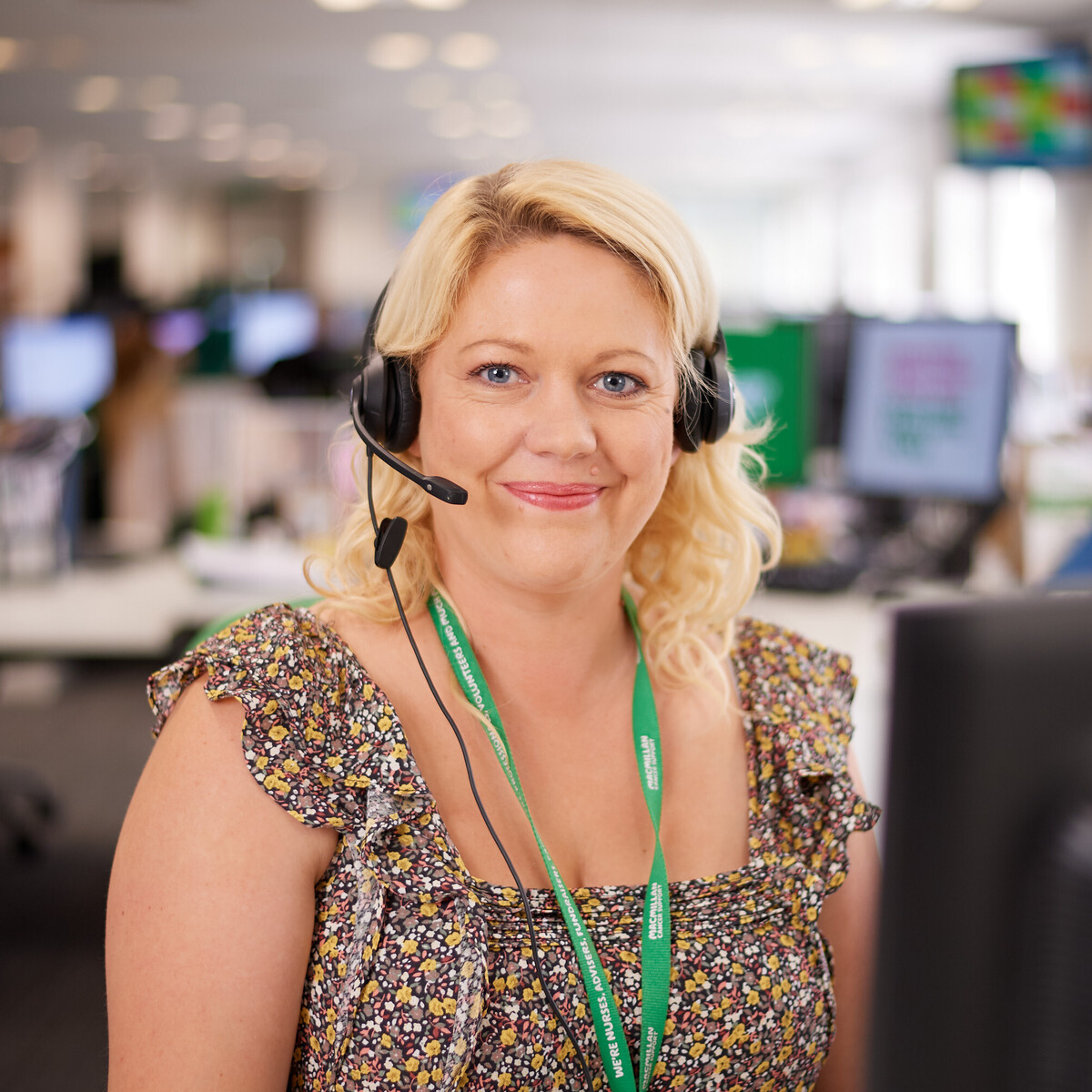 A woman sitting in front of a computer wearing a microphone headset looking at the camera.