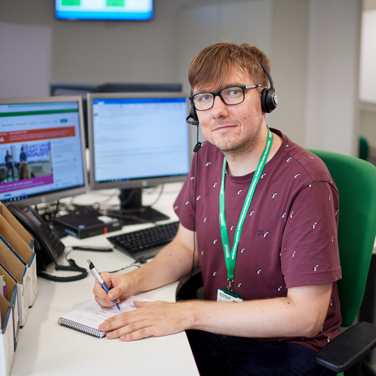 A man sitting in front of a computer wearing a microphone headset looking at the camera.