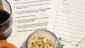 A bowl of cashews and a pen on some quiz sheets