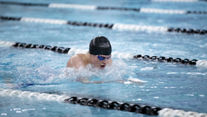 A man swimming the breaststroke in pool lanes. He is wearing goggles and a swim cap.