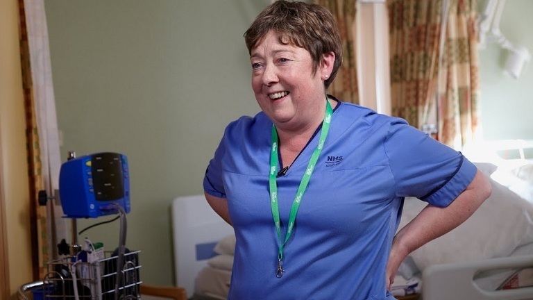 A smiling Macmillan healthcare professional wearing blue scrubs.