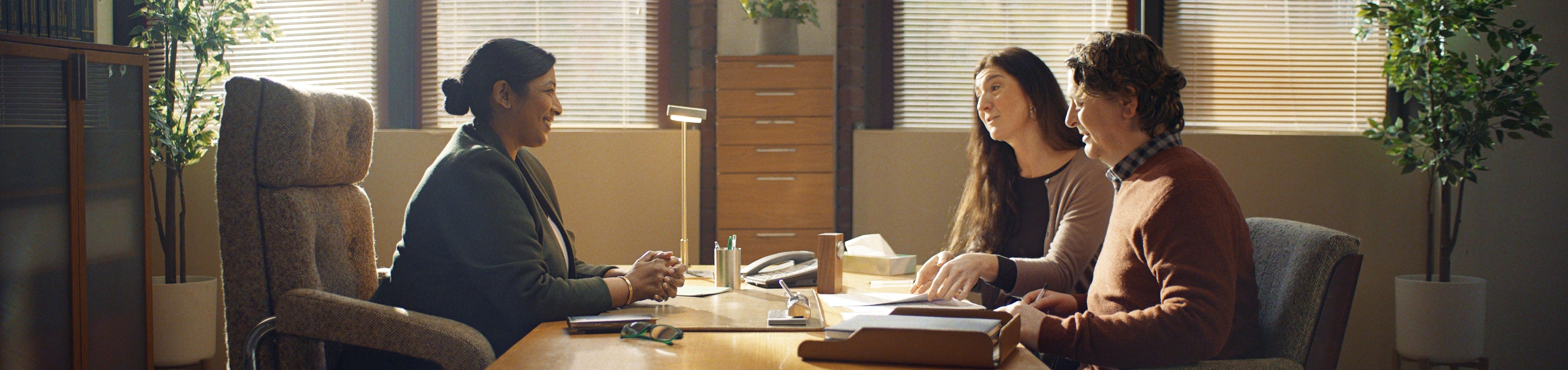 Two people sitting across a desk from a legal professional discussing their will.