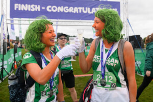 Two women in oompa loompa fancy dress saying cheers with bubbly at the finish of an outdoor event.