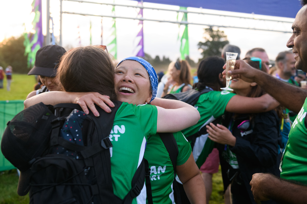 Two women hugging at the finish line of an outdoor event.