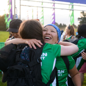 Two women hugging at the finish line of an outdoor event.