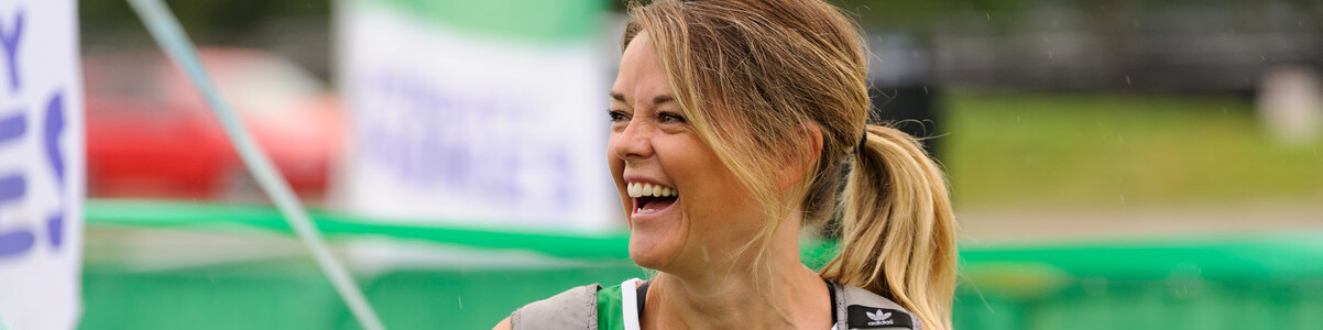 A woman at a fundraising event wearing a green, Macmillan running vest. She's looking away from the camera and smiling.