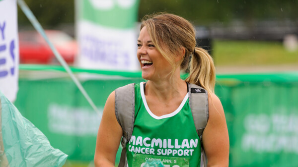 A woman at a fundraising event wearing a green, Macmillan running vest. She's looking away from the camera and smiling.