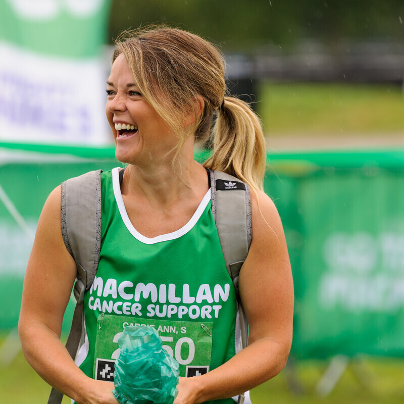 A woman at a fundraising event wearing a green, Macmillan running vest. She's looking away from the camera and smiling.