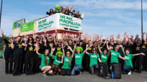 Macmillan supporters and members of Rock Choir in front of an open top bus decorated in Macmillan flags.