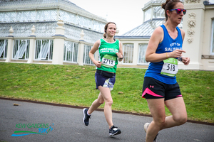 A woman in a green Macmillan running vest runs past the conservatory at Kew Gardens.