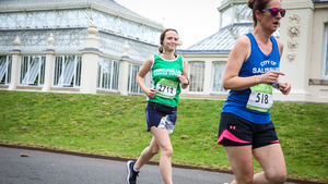 A woman in a green Macmillan running vest runs past the conservatory at Kew Gardens.