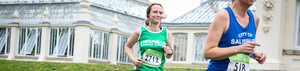 A woman in a green Macmillan running vest runs past the conservatory at Kew Gardens.