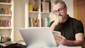 A man sitting at a table looking at a tablet and a laptop in front of him