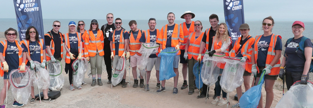 SUEZ employees standing together in orange high vis vests. They are litter picking.