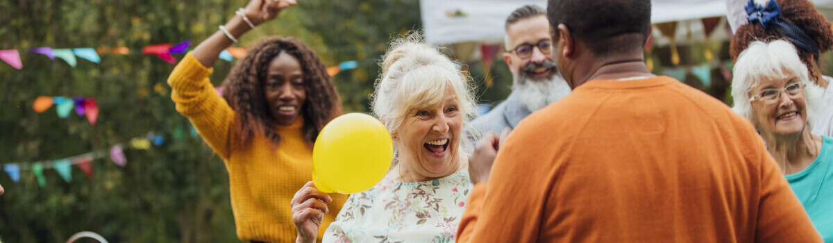 A woman smiles and dances with a man in garden. There are other people dancing in the background and there is bunting hanging.