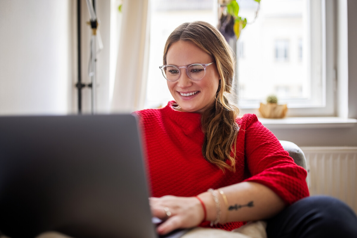 A white woman wearing glasses is smiling and typing on her laptop.