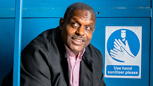 Errol, who was diagnosed with prostate cancer. He is sitting on a metal staircase in front of a blue wall. He is using a tablet device.