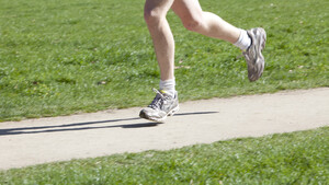 Close-up of a man's legs running on a path in a park