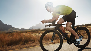 A man cycling along a road with mountains in the bakground.