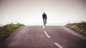 A man cycling over the brow of a hill on a countryside road.