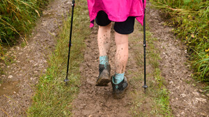 The back of a hiker's muddy legs walking along a muddy path