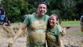 A muddy couple standing with their arms around eachother smiling after a tough race.