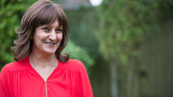 Ravinder, a Macmillan volunteering ambassador. Ravinder is wearing a red top and standing in front of trees.