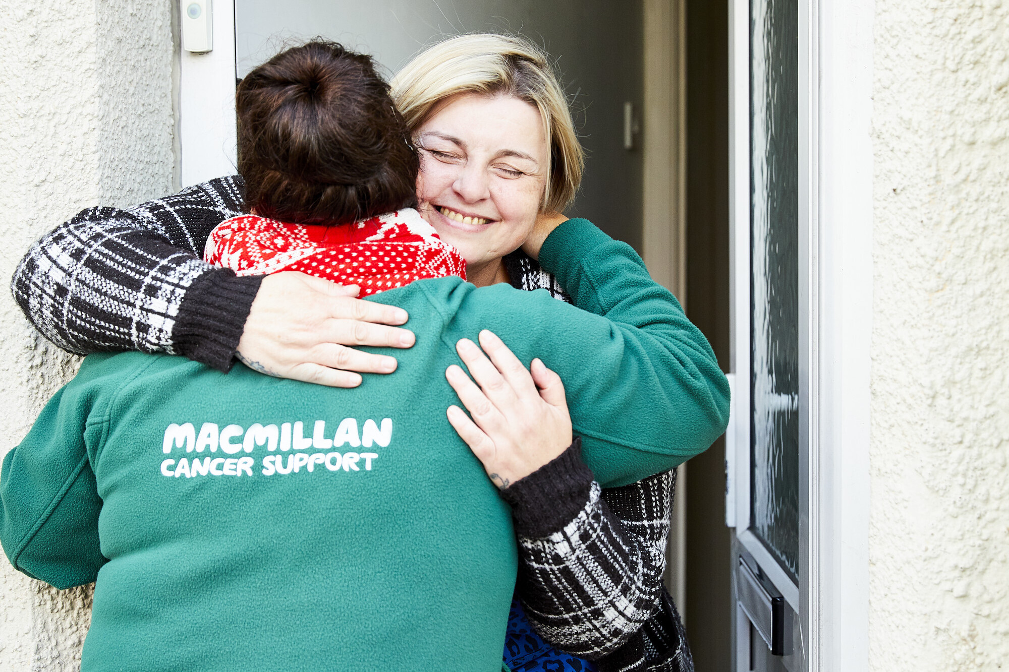 Clare welcoming a Macmillan Professional at her front door, chatting with Macmillan Professionals in her home, preparing food.
