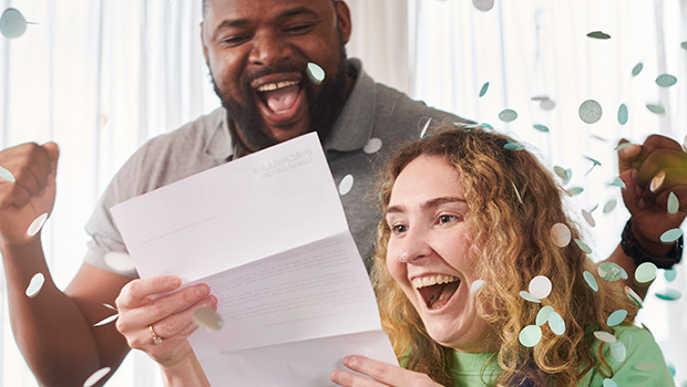 A couple celebrating and smiling while reading a letter and confetti in the background
