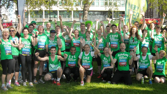 Lots of Team Macmillan runners standing together cheering with their arms in the air.
