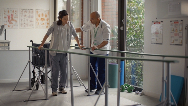 A nurse helping a patient to walk through parallel rails