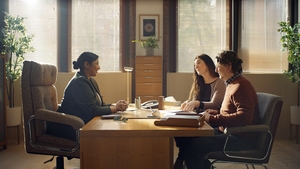 Two people sitting across a desk from a legal professional discussing their will.