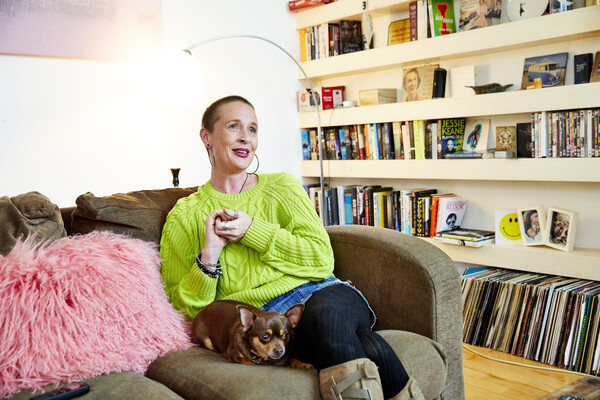 White lady smiling sat on sofa with pet dog sat next to her.